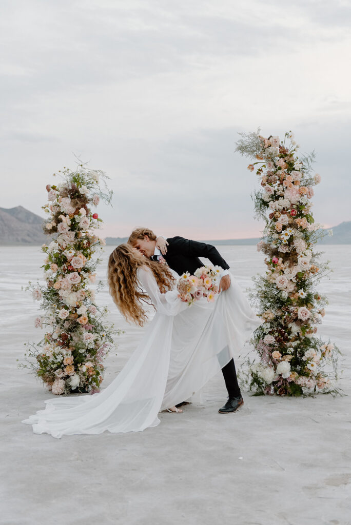 dip kiss at gorgeous floral arch during their salt flats elopement