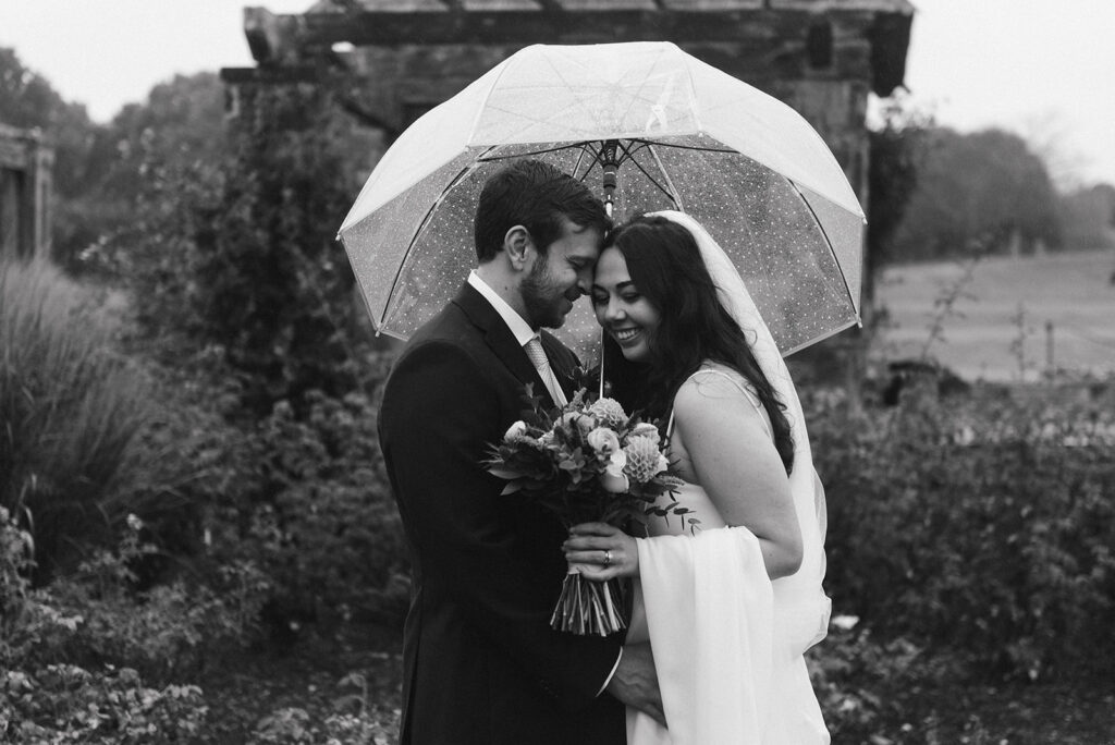bride and groom hiding from the rain under a clear umbrella during their rainy elopement day
