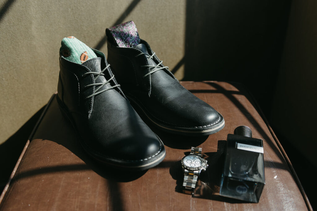 groom elopement details of black shoes, perfume, watch and colorful socks